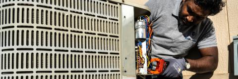 Photo of a technician working on an HVAC unit with hand tools outdoors